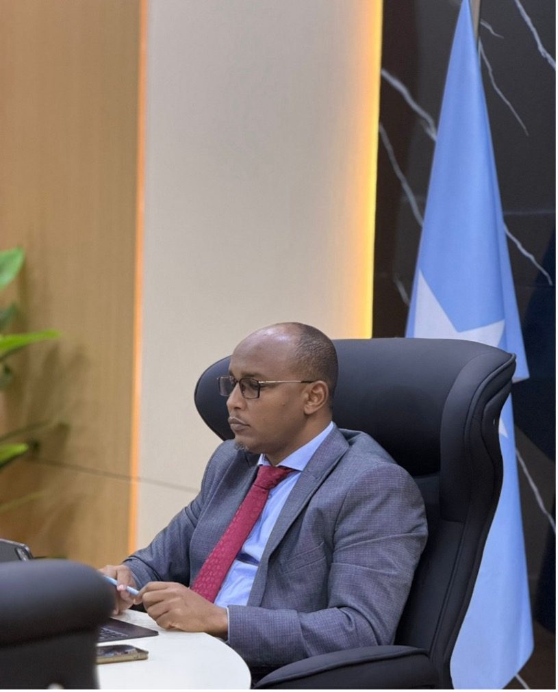 Dr Mohamed Mohamud Mohamed, Rector of Somali National University, seated at his desk beside the Somali national flag